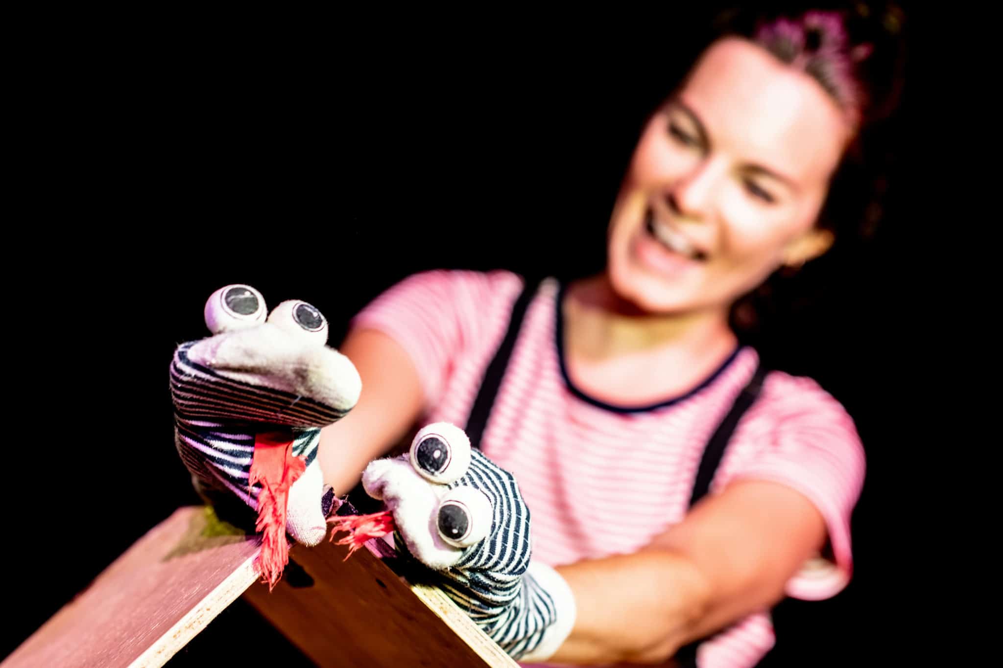 Fotografi: Bildet viser en kvinne som spiller dukketeater. Dukkene er på hånden hennes og skal forestille to slanger med geipende, rød tunge.
