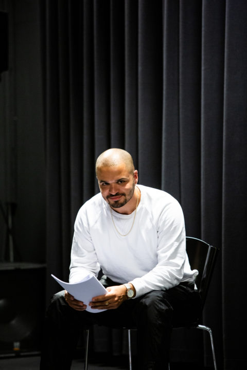 Fotografi. Bildet viser et portrettbilde av Julian Karenga. Han sitter på en stol med et manuskript i hånden.