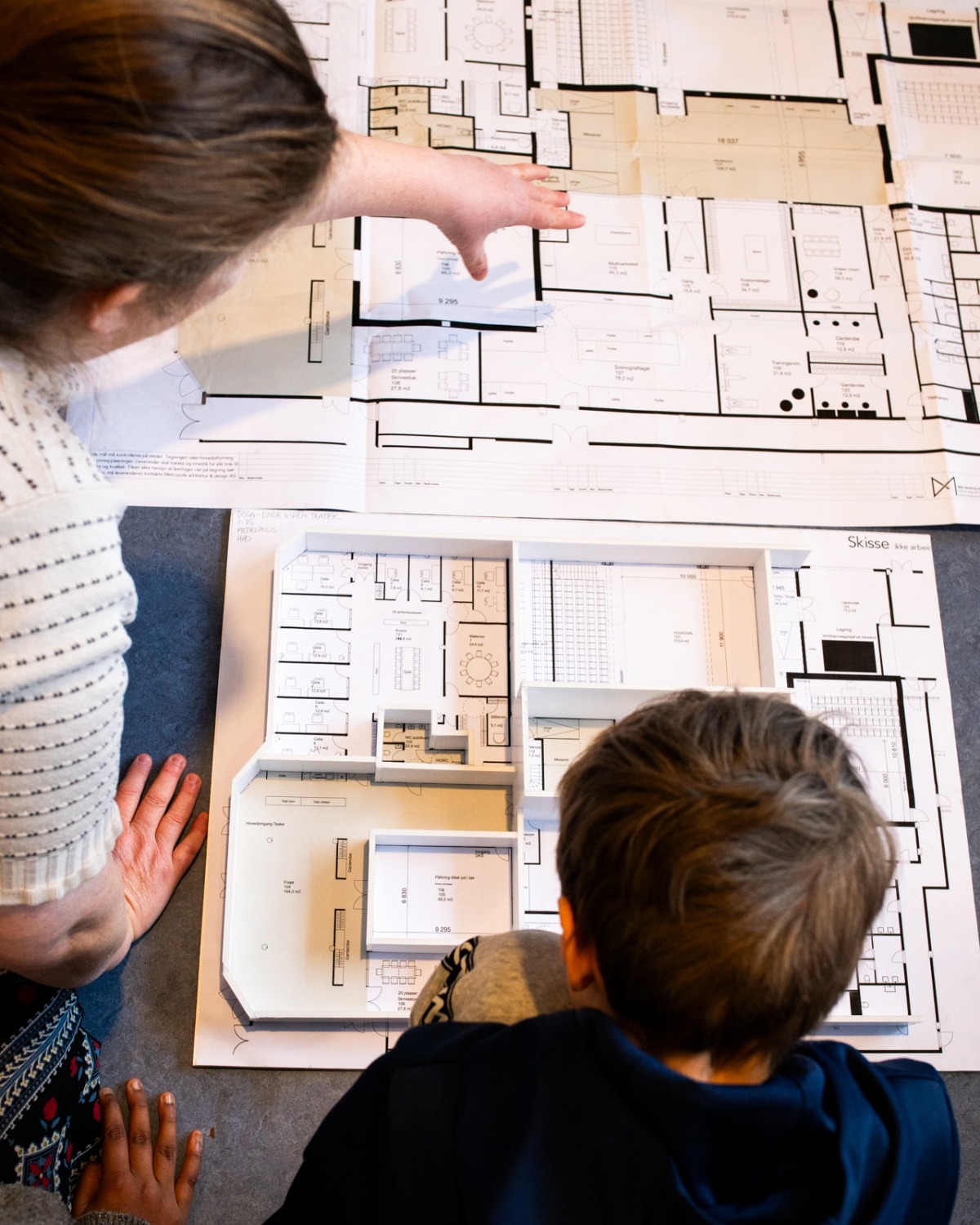 Interiørarkitekten og en gutt i 12årsalderen ser på en papirmodell av det nye bygget sammen.