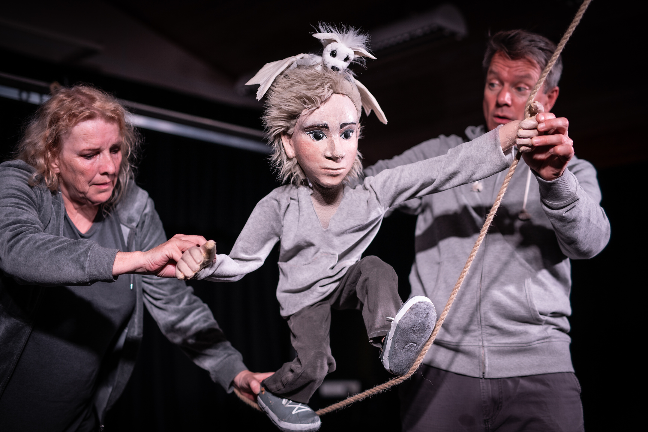 Fotografi: Bildet viser to skuespillere som fremfører med en dukke. Alle er ikledd gråe klær.